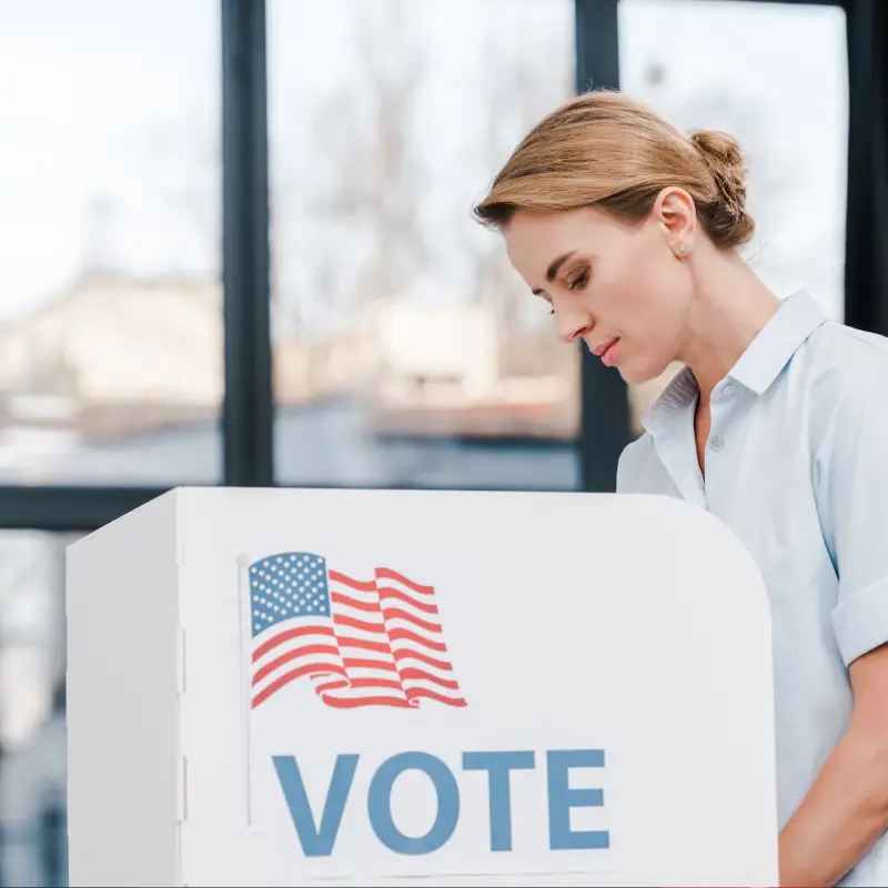 side view of attractive woman voting near stand with vote lettering and american flag<br />
