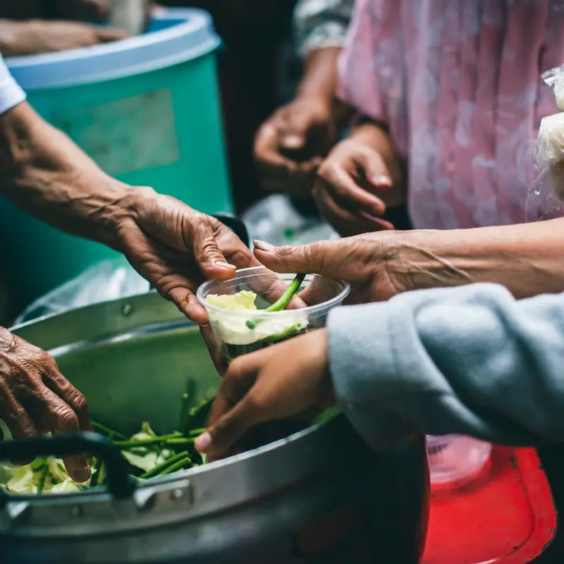 A volunteer serves food from a large pot to a person